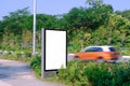 Advertising billboard by the road, with passing speeding car in motion blur. Blank vertical mock up template for out-of-home OOH