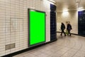 Advertising board display green mockup on wall with white tiles at underground station passage, blurred people in background