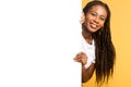 Advertising concept. Smiling attractive black woman peeking out from behind white empty paper poster Royalty Free Stock Photo
