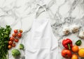 Advertising shot of kitchen white fabric apron, cook uniform, protection apparel on marble table with vegetables and