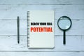 Advice and motivation. Top view of pen,magnifying glass and notebook written with Reach Your Full Potential on white wooden