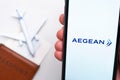 Aegean Airline app on a smartphone screen in mans hand. A toy plane, passport and tickets are on the table. November