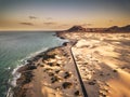 Aerial above view of yellow tropical sandy beach with black long way road and car traveling - ocean blue waves and shore - sunset Royalty Free Stock Photo