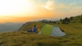 AERIAL: Active young couple sitting by their tent and watching the sunset.