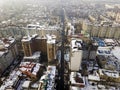 Aerial black and white winter top view of modern city center with tall buildings and parked cars on snowy streets