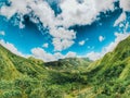 Aerial bright shot of green mountains and a palms field with a cloudy clear sky in the background