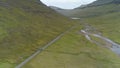 AERIAL: Car driving down a scenic narrow straight road approaching a remote lake