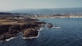 Aerial coast view of rocks and ocean waves with little town in background. Blue sky and ocean waves with windmills and mountains. Royalty Free Stock Photo