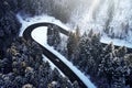 Aerial drone view of a curved winding road through the forest high up in the mountains in the winter with snow covered Royalty Free Stock Photo