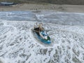 Aerial drone view of fishing ship stranded and stuck in shallow water at the coastline.