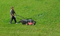 Aerial drone view of gardener mowing overgrown lawn with motorized lawnmower in the garden. Landscaping service, gardening