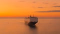 AERIAL: Drone view of a massive cargo carrier sailing across the sea at sunset.