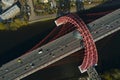 Aerial drone view on modern urban red cable arch bridge with many automobiles, cars, trucks on road above river. Scenic bridge