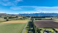 Aerial farming grazing and crop fields in rural countryside with a backdrop of the snow capped Mountain range under clear skies