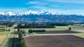 Aerial farming pasturte and crop fields in rural countryside with a backdrop of the snow capped Mountain range under clear skies