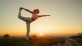 AERIAL: Flexible Caucasian woman holds a scorpion pose in front of the sunset.