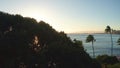 Aerial flight straight from behind between palm trees above water in ocean against colorful sunset. Panning aerial drone Royalty Free Stock Photo