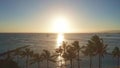 Aerial flight straight from behind between palm trees above water in ocean against colorful sunset. Panning aerial drone Royalty Free Stock Photo