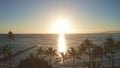 Aerial flight straight from behind between palm trees above water in ocean against colorful sunset. Panning aerial drone Royalty Free Stock Photo