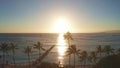 Aerial flight straight from behind between palm trees above water in ocean against colorful sunset. Panning aerial drone Royalty Free Stock Photo