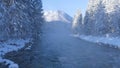 AERIAL: Flying above the misty forest stream running towards the snowy mountain. Royalty Free Stock Photo