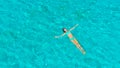 AERIAL: Flying above relaxed tourist girl floating on the glassy ocean water.