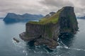 AERIAL: Flying around a grassy islet with black rocky cliffs towering over sea. Royalty Free Stock Photo