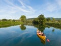 AERIAL: Flying behind tourists canoeing along calm river running past a church Royalty Free Stock Photo