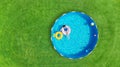 Aerial. Girl swims in a metal frame pool with inflatable toys. Frame pool stand on a green grass lawn. Top view.