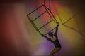 Aerial gymnast in black leotard on multicolored background of studio. Female acrobat performing on a cube, performing