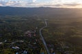 Aerial landscape of 4 lane road with residential area, forest, mountain, blue sky and sunlight with high angle view of main road