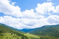 Landscape with mountains, green trees, field, road and river under blue sky and clouds in summer Royalty Free Stock Photo