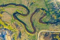 Aerial landscape of winding small river, stream in green field, top evening sunset view meadow