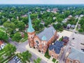 Aerial of a large church with a rusted copper spiral in the sky surrounded by little building and trees