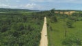 AERIAL: Lonely white van drives down tropical dirt road towards busy gravel pit.