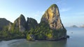 AERIAL: Massive rocky cliff providing shade for the tranquil white sandy beach.