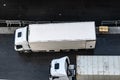 Aerial/Overhead view of two white 6 wheeler delivery trucks parked side by side on asphalt road.