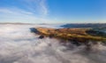 Aerial panorama of a narrow, winding mountain road emerging above a bank of fog in a rural valley