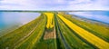 Aerial Panorama of rural road passing through vivid yellow canola fields between two lakes. Royalty Free Stock Photo