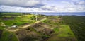 Aerial panorama of stormy clouds above wind turbines and pastures on ocean shore.