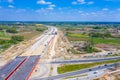 Aerial panorama top down view of an unfinished asphalt covered road with dirt, tracks of heavy machinery at construction site. The