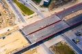 Aerial panorama top down view of an unfinished asphalt covered road with dirt, tracks of heavy machinery at construction site. The