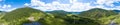 panoramic banner view of landscape with mountains, green trees, field, road and river under blue sky and clouds in summer Royalty Free Stock Photo