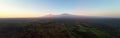 Aerial, panoramic view on Mount Kilimanjaro volcano, summit covered in snow lit by first sun rays with masai villages with