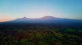 Aerial, panoramic view on Mount Kilimanjaro volcano, summit covered in snow lit by first sun rays with masai villages with