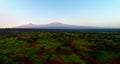 Aerial, panoramic view on Mount Kilimanjaro volcano, summit covered in snow lit by first sun rays with masai villages with