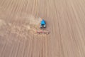 Aerial perspective view on blue tractor pulling a plow, preparing a soil for seed sowing, tractor making dirt cloud