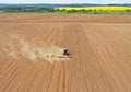 Aerial perspective view on blue tractor pulling a plow, preparing a soil for seed sowing, tractor making dirt cloud. Landmark on