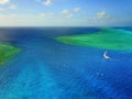 Aerial photo of a sailboat navigating through a tropical pass between reefs