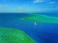 Aerial photo of a sailboat navigating through a tropical pass between reefs